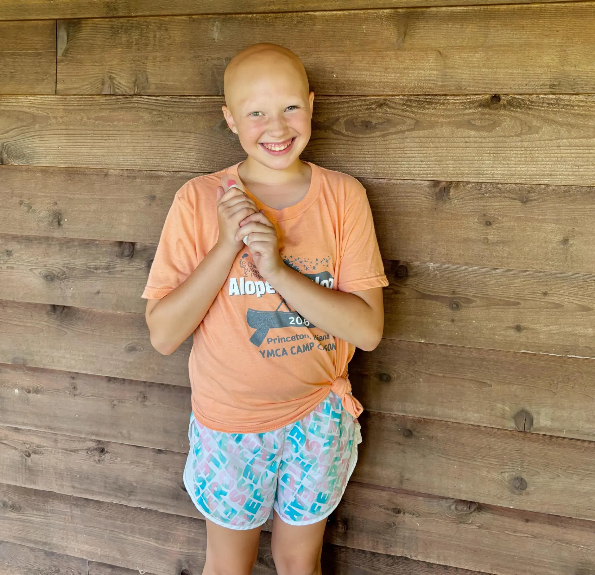 Alopeciapalooza camper in an orange 2026 camp t-shirt